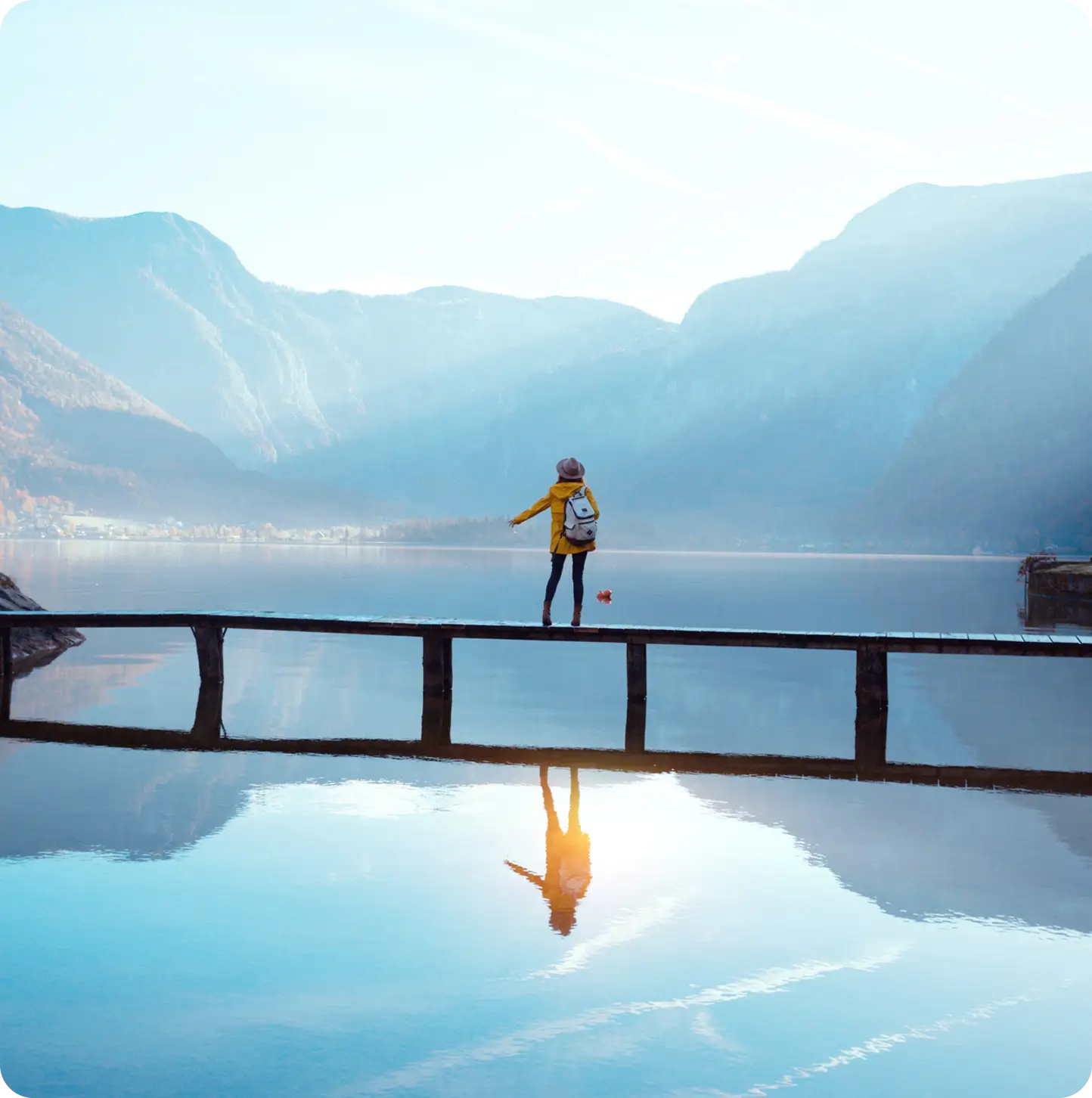 A woman balancing on a narrow dock over a serene mountain lake.